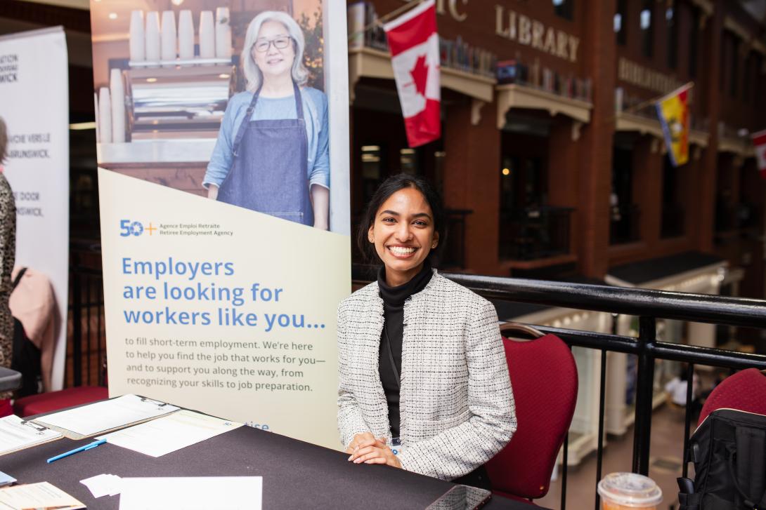 Individual sitting at a booth at a job fair smiling