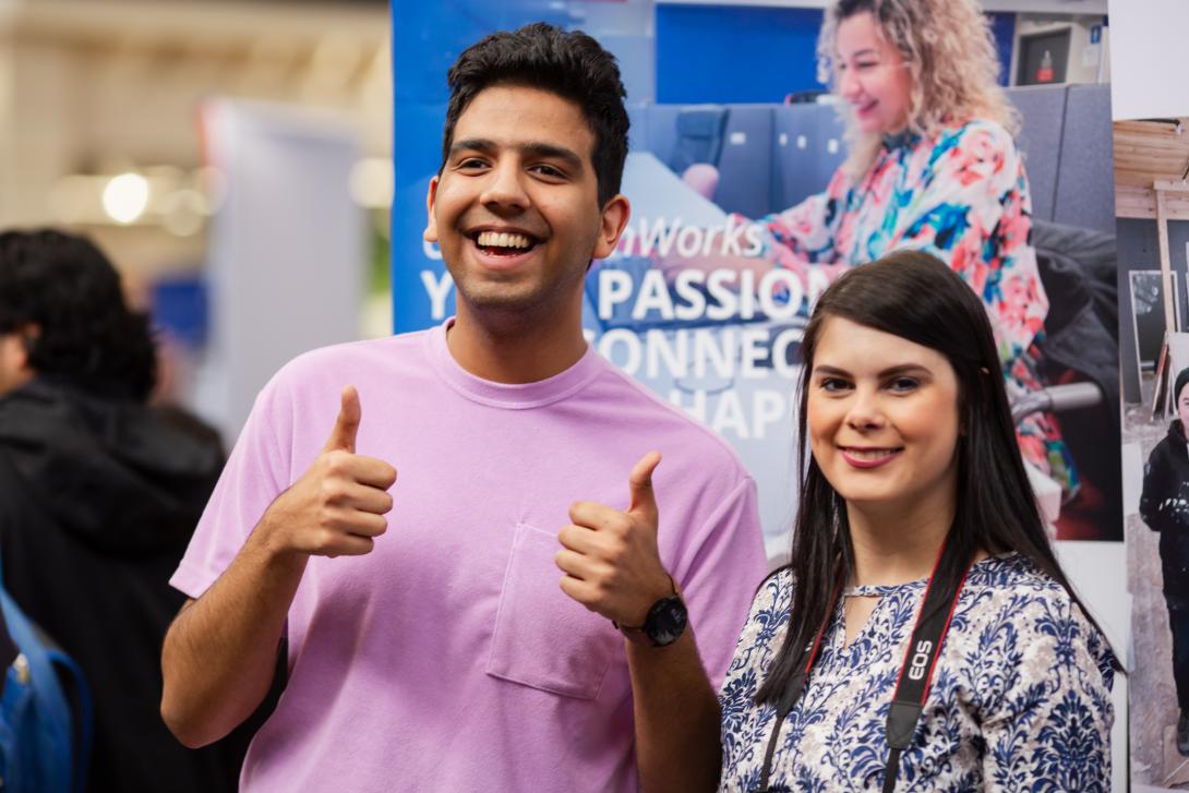 Two people standing by a banner smiling